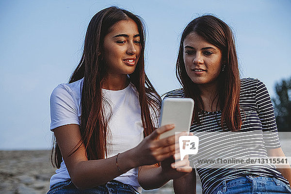 Freundinnen schauen auf Smartphone gegen den Himmel in der Stadt