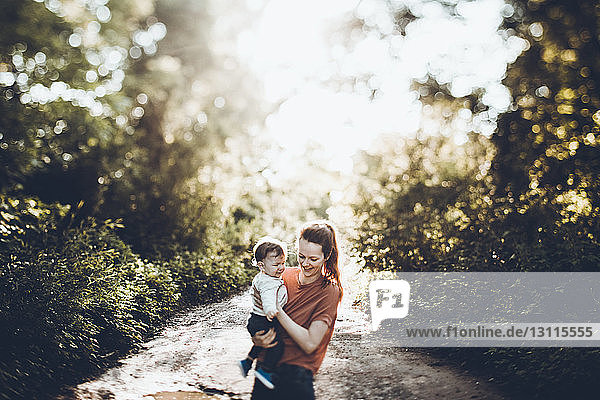 Mutter trägt einen Sohn  während sie auf einem Feldweg im Wald steht