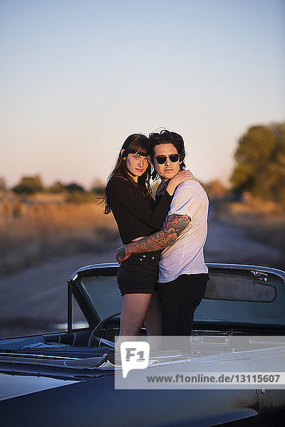 Couple embracing while standing in convertible against clear sky