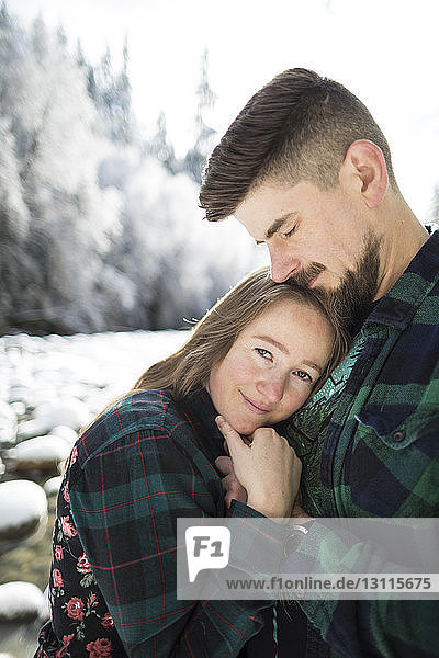 Portrait of smiling woman embracing man at Lynn Canyon Park during winter