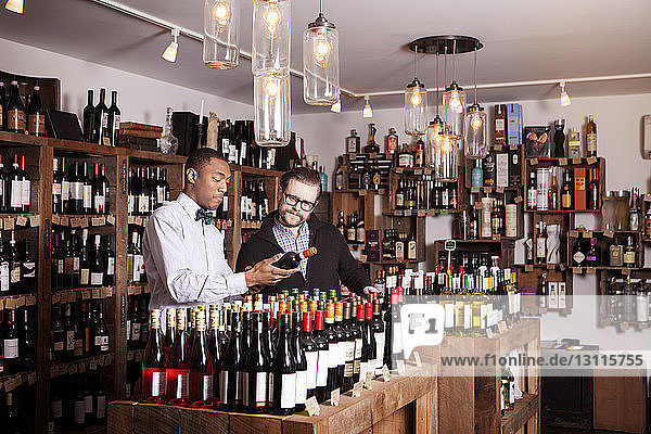 Männliche Kollegen lesen Etikett auf Weinflasche im Geschäft