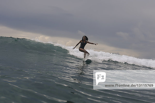 Frau surft auf dem Meer vor bewölktem Himmel