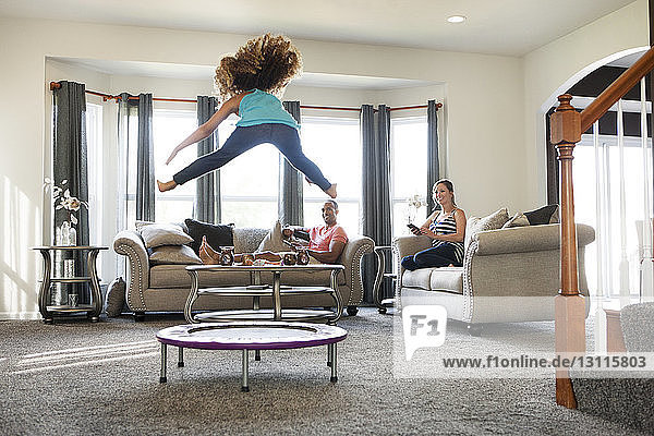 Parents watching daughter jumping on trampoline at home