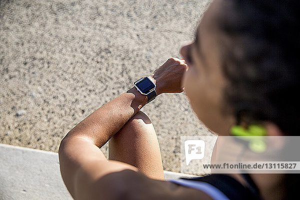 Hochwinkelansicht einer Sportlerin  die eine intelligente Uhr trägt  während sie im Park sitzt