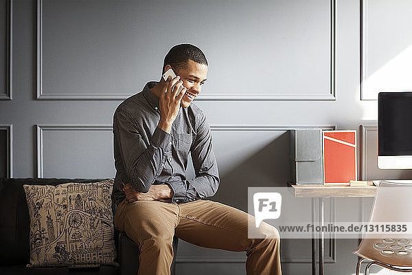 Businessman using smart phone while sitting on sofa in office