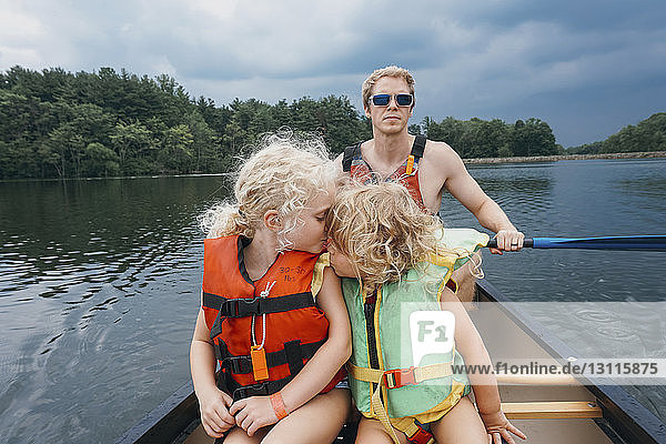Sister kissing girl while father canoeing in lake against stormy clouds
