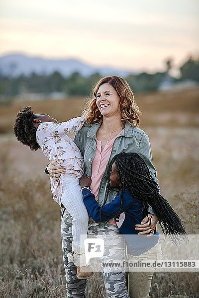 Smiling mother playing with daughters while standing on grassy field at forest