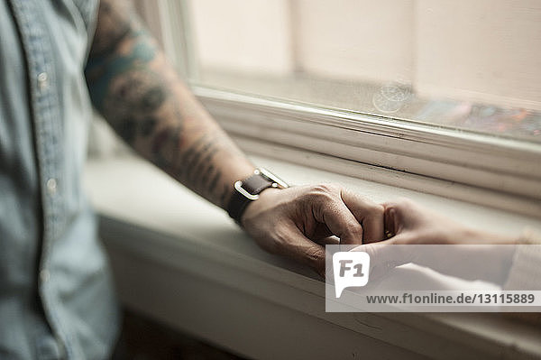 Ausschnitt eines Paares  das zu Hause auf dem Fensterbrett Händchen hält