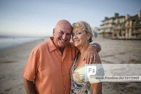 Portrait of smiling senior couple standing at beach against sky