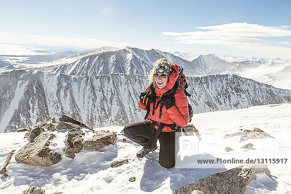Glückliche Frau kniet auf schneebedecktem Berg gegen den Himmel