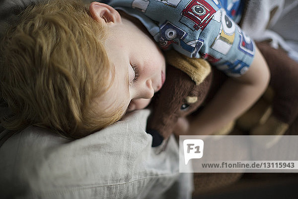 Junge mit Teddybär schläft zu Hause auf dem Sofa