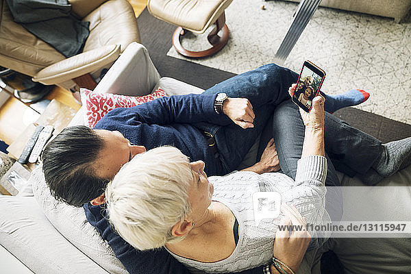 Hochwinkelansicht eines älteren Ehepaars bei Videokonferenzen  während es zu Hause auf dem Sofa sitzt