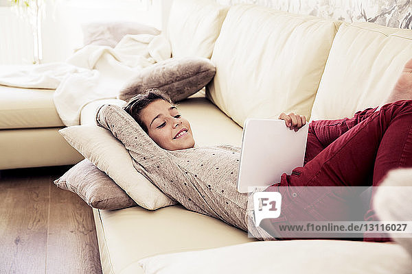 Lächelndes Mädchen betrachtet digitales Tablett im Liegen auf dem Sofa