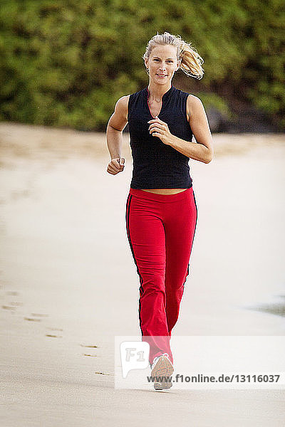 Lächelnde Frau in voller Länge am Strand joggend