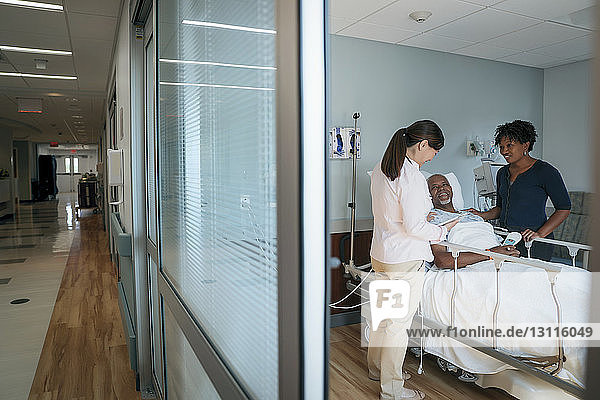 Female doctor talking with senior patient and woman in hospital ward seen through doorway
