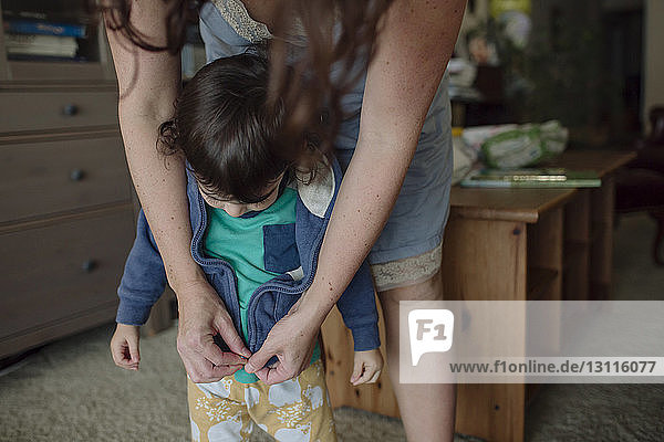Midsection of mother dressing daughter while standing at home