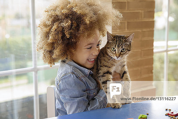 Mädchen spielt zu Hause mit Katze auf dem Tisch