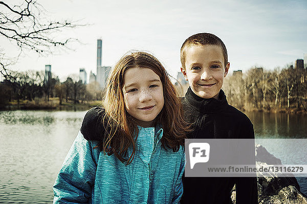 Portrait of smiling brother with arm around sister at lake in park