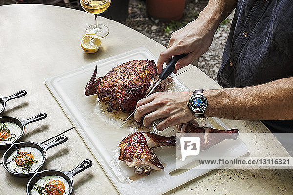Midsection of man cutting roasted chicken on table at backyard