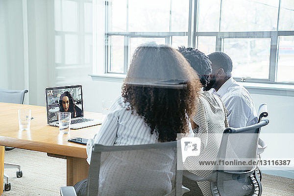 Geschäftsleute Videokonferenz mit Geschäftsfrau über Laptop-Computer im Sitzungssaal durch Glas gesehen