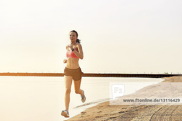 Weibliche Sportlerin joggt am Ufer vor klarem Himmel