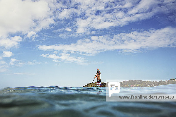 Man paddleboarding in sea against sky