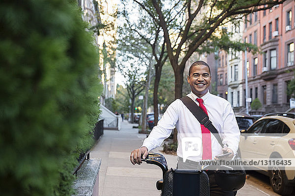 Portrait of happy businessman standing with bicycle on footpath