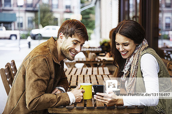 Glückliches Paar schaut auf Handy  während es Getränke im Café genießt