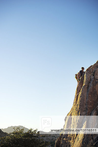 Tiefwinkelansicht eines Mannes  der am Fels klettert  bei strahlend blauem Himmel während eines sonnigen Tages