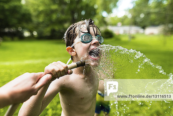 Junge ohne Hemd mit Schwimmbrille beim Spielen mit Wasser im Hof