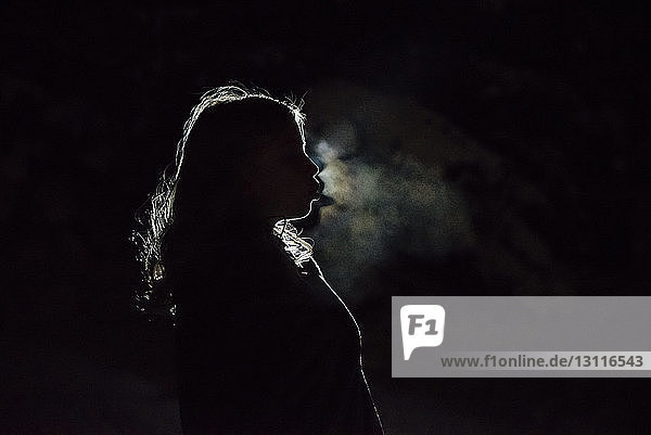 Seitenansicht eines Mädchens  das Rauch bläst  während es in der Dunkelkammer steht