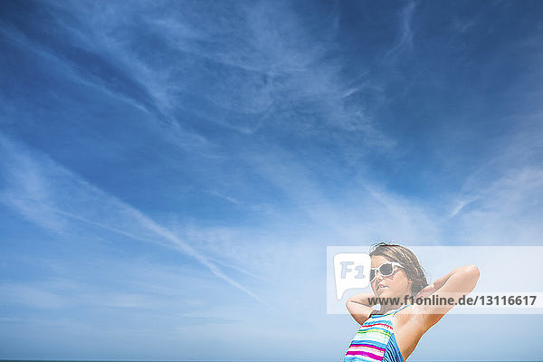 Niedrigwinkelansicht eines Mädchens mit Sonnenbrille vor bewölktem Himmel
