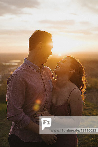 Fröhliches junges Paar steht bei Sonnenuntergang auf dem Feld