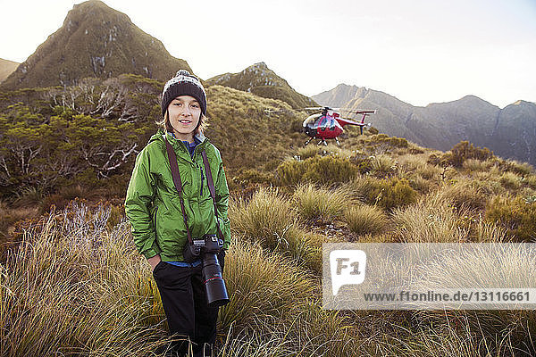 Portrait of boy with camera standing on mountain against helicopter