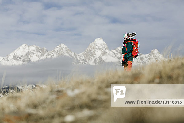 Seitenansicht einer Wanderin mit Rucksack  die vor schneebedeckten Bergen und bewölktem Himmel steht