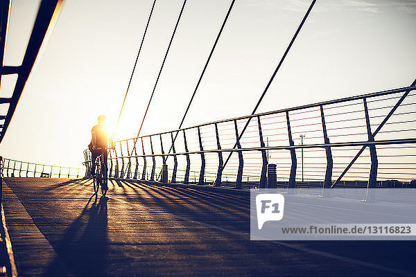 Mann fährt bei Sonnenschein auf Brücke gegen klaren Himmel