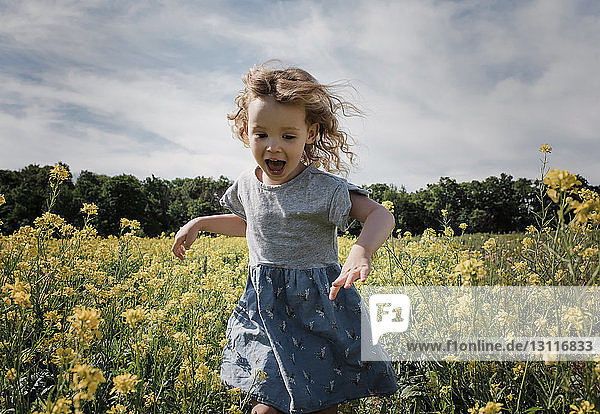 Glückliches Mädchen rennt stehend inmitten von Pflanzen gegen bewölkten Himmel