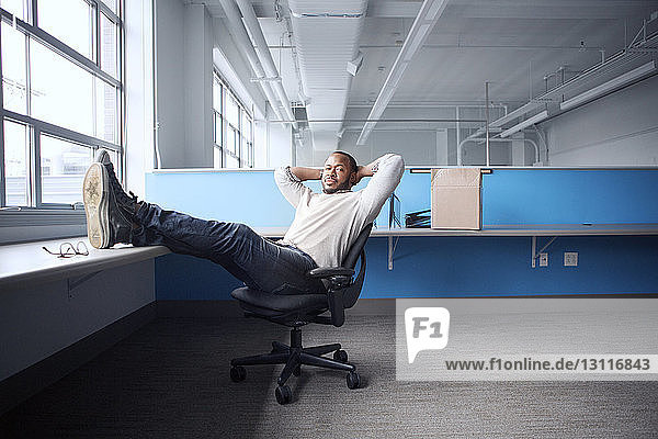 Porträt eines selbstbewussten Geschäftsmannes mit Händen hinter dem Kopf auf einem Stuhl im Büro sitzend