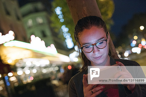 Junge Frau benutzt Smartphone in beleuchteter Stadt bei Nacht