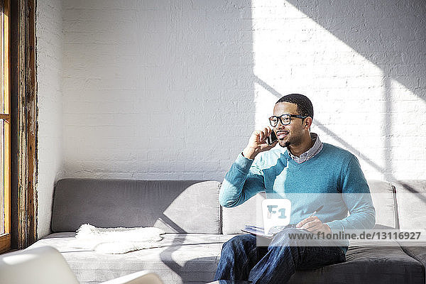 Geschäftsmann spricht mit dem Handy  während er im Büro auf dem Sofa sitzt