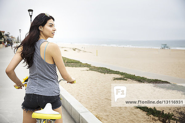 Rückansicht einer Fahrrad fahrenden Frau auf einer Brücke am Strand