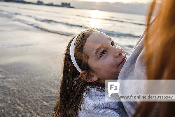 Tochter umarmt Mutter  während sie bei Sonnenuntergang am Strand steht