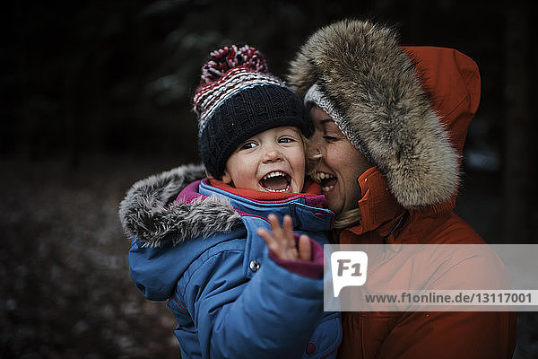 Glückliche Mutter trägt ihre Tochter  während sie im Winter im Wald steht
