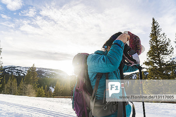 Frau trägt Strickmütze  während sie auf verschneitem Feld gegen den Himmel steht