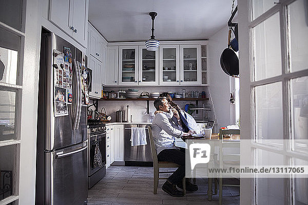 Tochter umarmt Vater mit Laptop-Computer in der Küche zu Hause