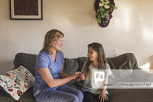 Hochwinkelansicht eines Arztes  der den Puls eines Mädchens prüft  während es zu Hause auf dem Sofa sitzt