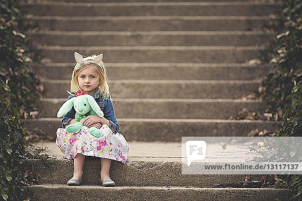 Portrait of cute girl holding stuffed toy sitting on steps