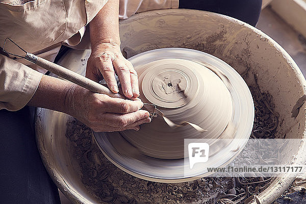 Hochwinkelansicht einer Frau  die mit einem Arbeitswerkzeug auf einer Töpferscheibe eine Form in Ton formt