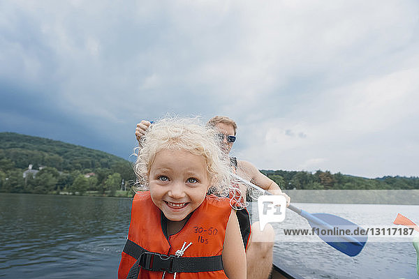 Happy daughter in canoe with father canoeing in background against stormy clouds