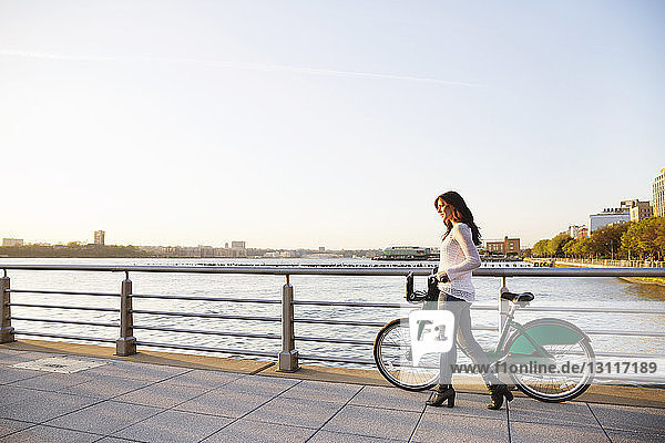 Seitenansicht einer Frau  die mit dem Fahrrad auf der Promenade bei klarem Himmel unterwegs ist